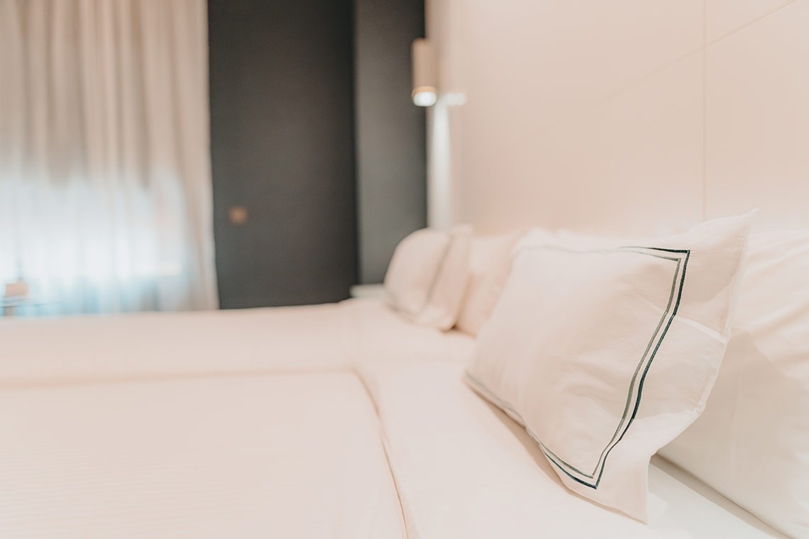 una cama con sábanas blancas y almohadas verdes