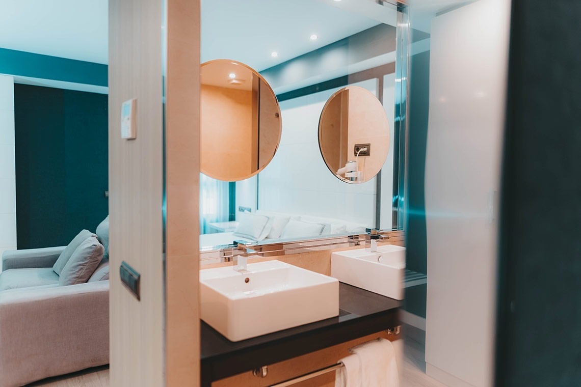 un baño con dos lavabos y un espejo redondo