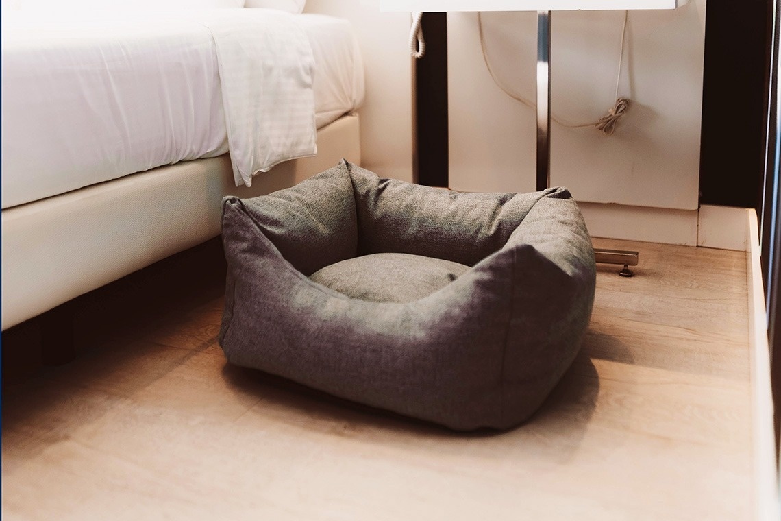a grey dog bed sits on the floor next to a bed
