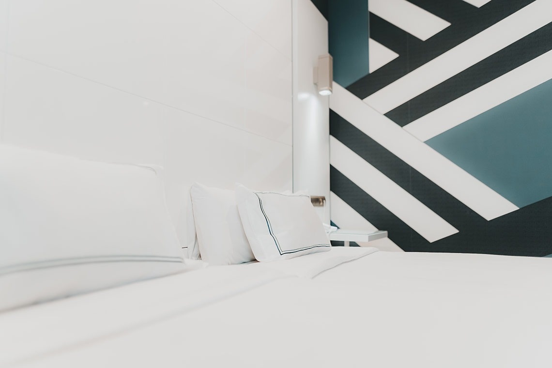 una cama con sábanas blancas y una pared a rayas negras y blancas