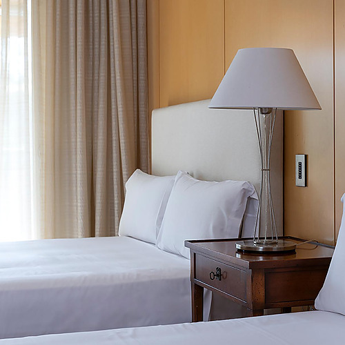 Lits jumeaux blancs et confortables dans une chambre d'hôtel, avec lampe de table et fenêtre. Suites del Mar Fenals Apartments