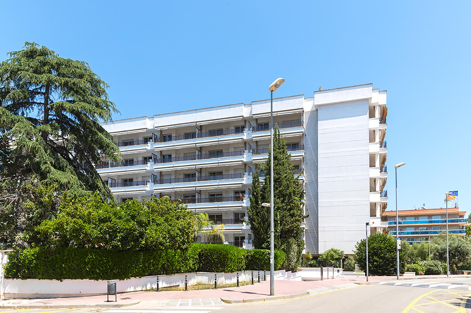 Edificio hotelero blanco con balcones y árboles verdes. Suites del Mar Fenals Apartments