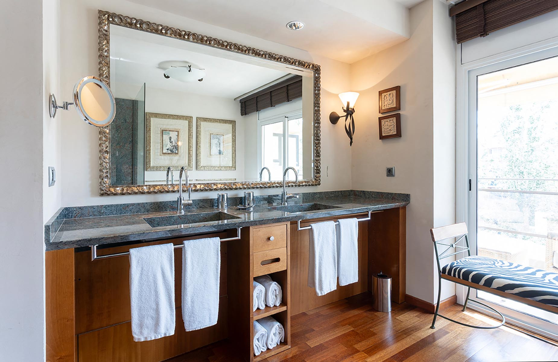 Luxury bathroom with double sinks, ornate mirror, and zebra-striped bench Suites del Mar Fenals Apartments.