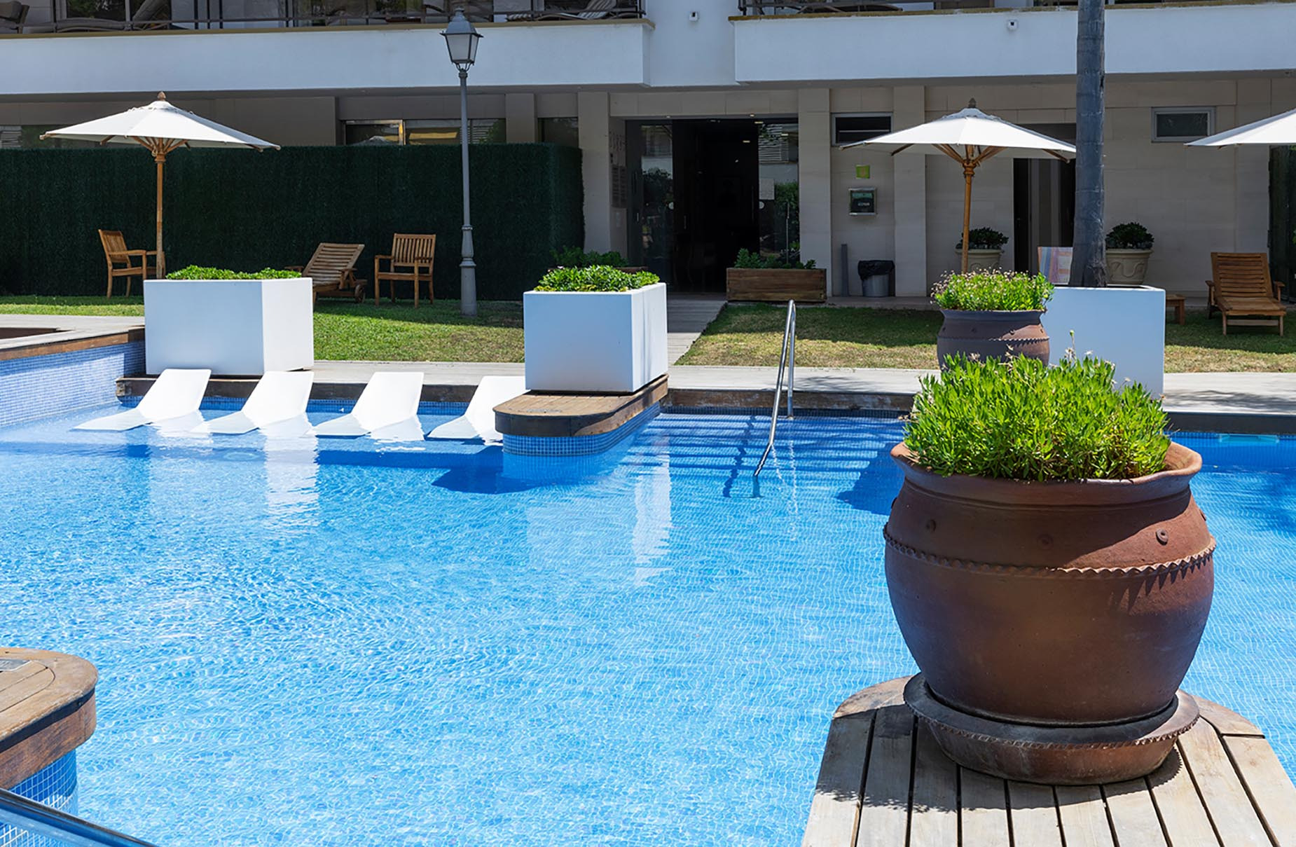 Terraza de piscina con tumbonas, sombrillas y plantas en @Suites del Mar Fenals Apartments@.