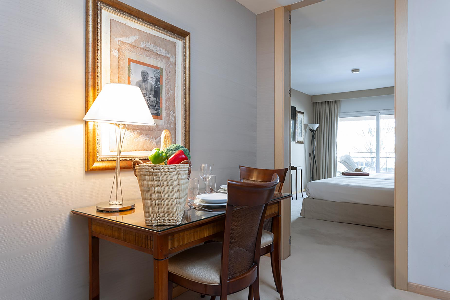 Elegant hotel dining area with a framed Buddha artwork, featuring a basket of produce and a glimpse into a Suites del Mar Fenals Apartments bedroom.