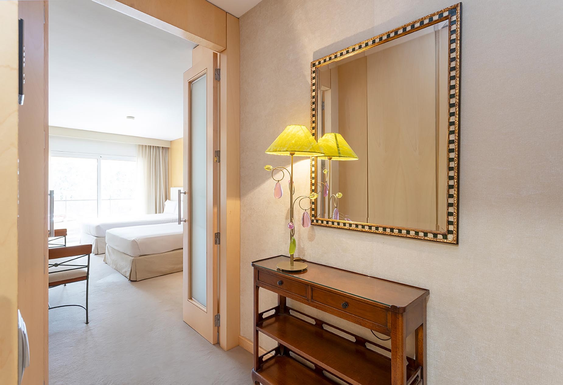 Hallway with mirrored console table and entrance to a Suites del Mar Fenals Apartments room with two beds.