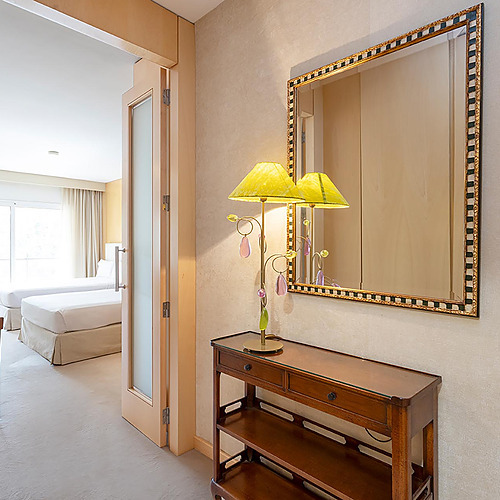 Console avec miroir et lampe à côté des portes d'une chambre d'hôtel avec deux lits. Suites del Mar Fenals Apartments