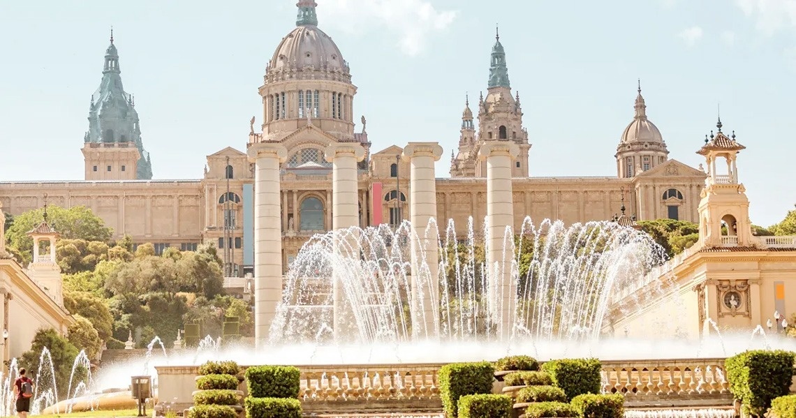 Vista aèria d'una ciutat costanera amb una platja extensa plena de gent, edificis a la vora i turons boscosos, amb nombroses embarcacions a les aigües blaves del mar.