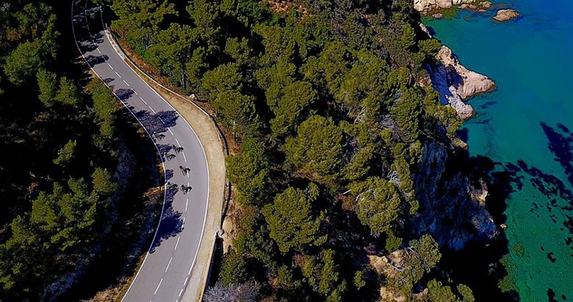 Vista aèria d'una ciutat costanera amb una platja extensa plena de gent, edificis a la vora i turons boscosos, amb nombroses embarcacions a les aigües blaves del mar.
