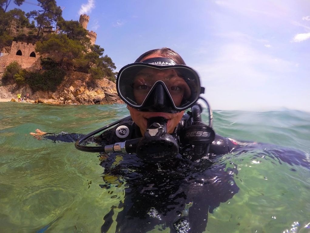 Une vue aérienne capture une ville côtière s'étendant le long d'une plage bondée, avec des bâtiments, des collines verdoyantes et une mer bleue parsemée de bateaux.