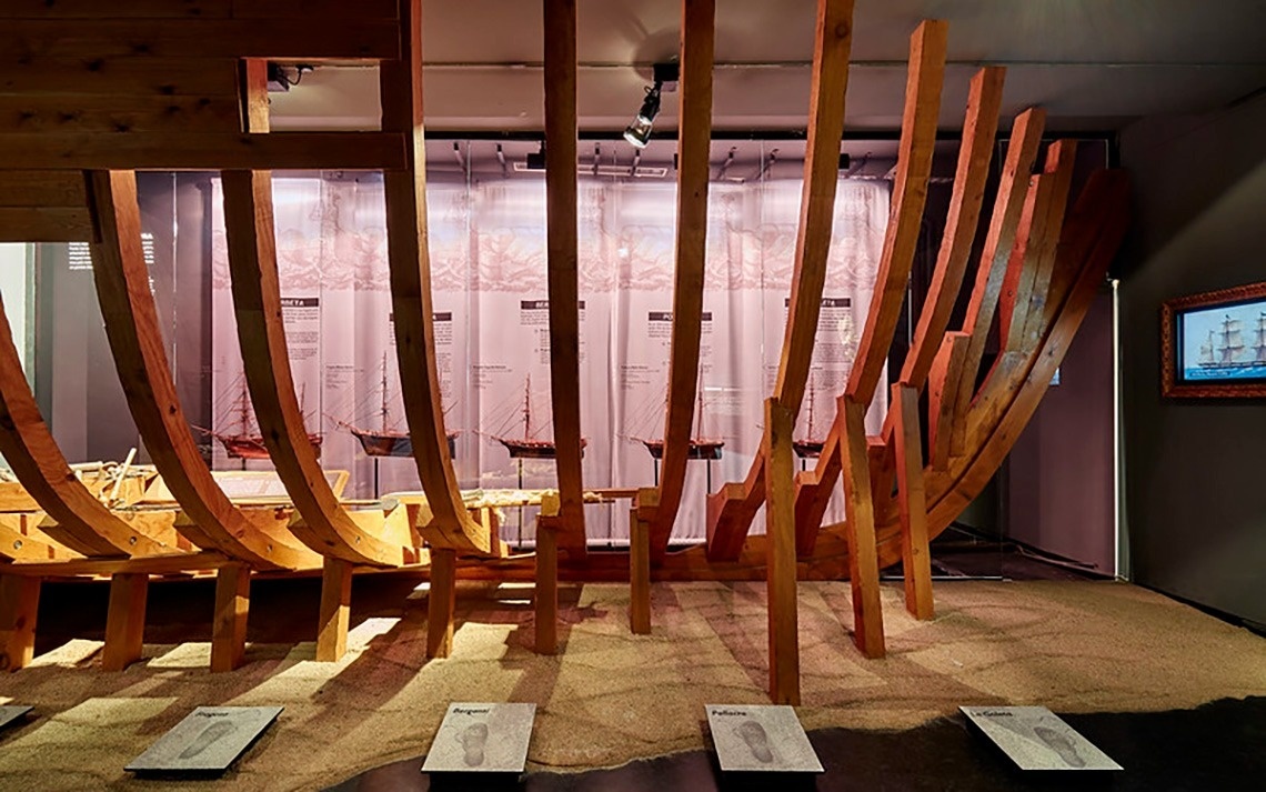 Vista aèria d'una ciutat costanera amb una platja extensa plena de gent, edificis a la vora i turons boscosos, amb nombroses embarcacions a les aigües blaves del mar.