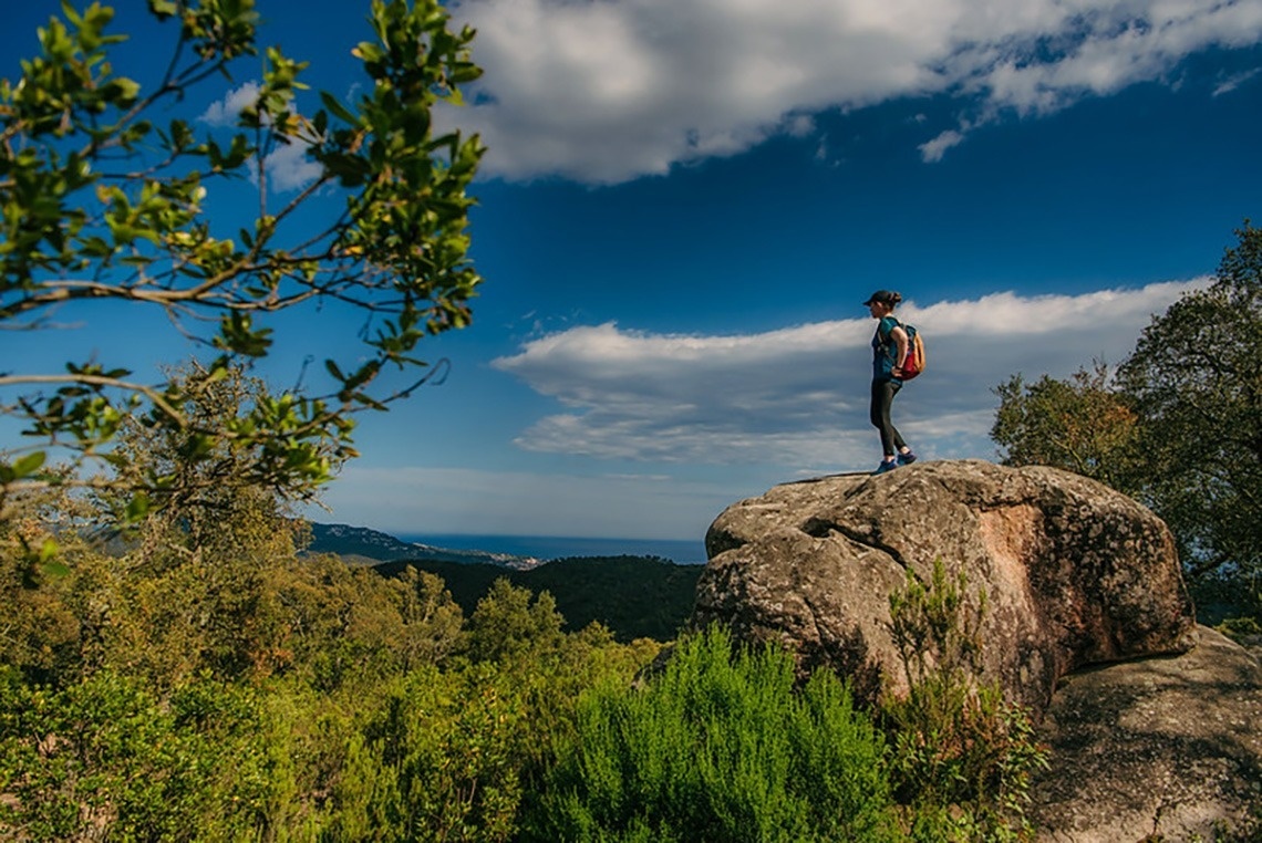 Vista aèria d'una ciutat costanera amb una platja extensa plena de gent, edificis a la vora i turons boscosos, amb nombroses embarcacions a les aigües blaves del mar.