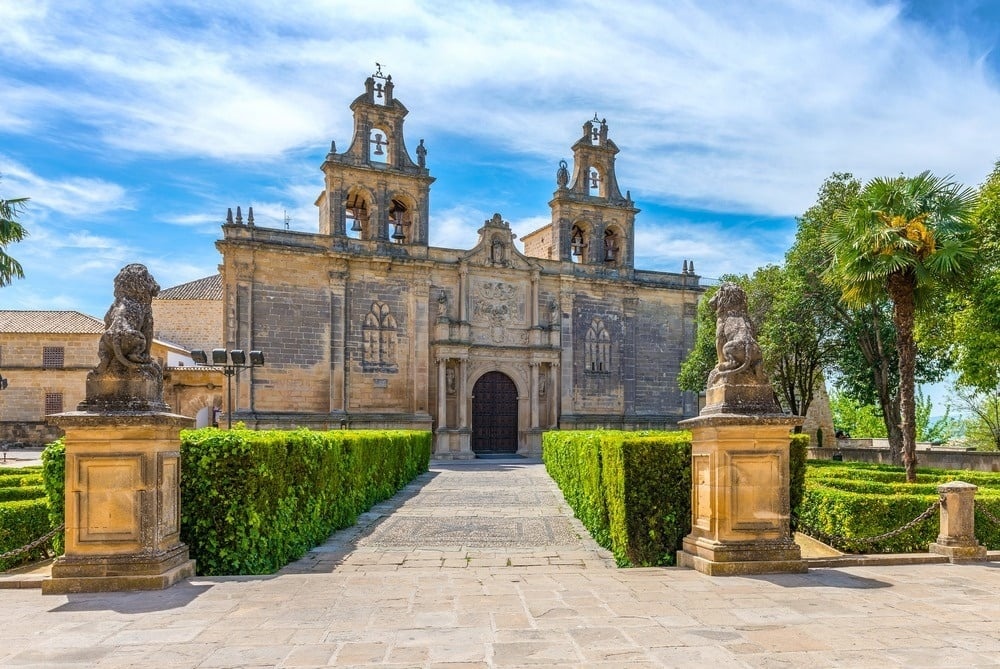 Hotel histórico con torres, fachada ornamentada, estatuas de leones y jardines exuberantes bajo cielo azul.