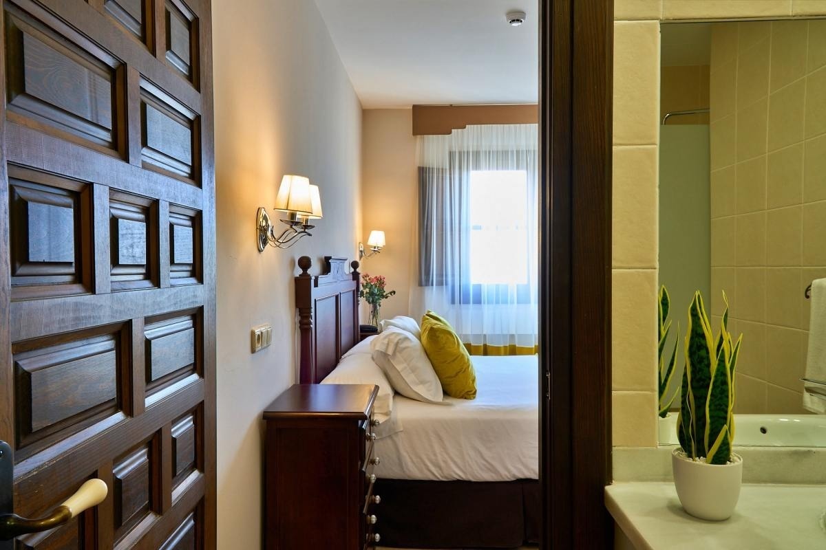 una puerta de madera conduce a una habitación con una cama y un espejo