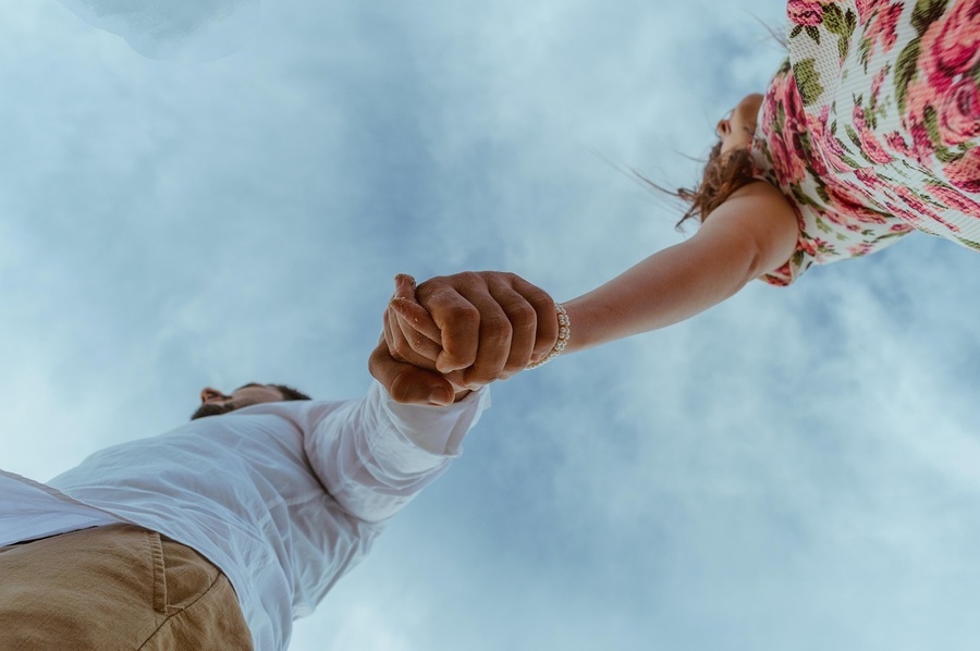 a man and a woman are holding hands against a cloudy sky