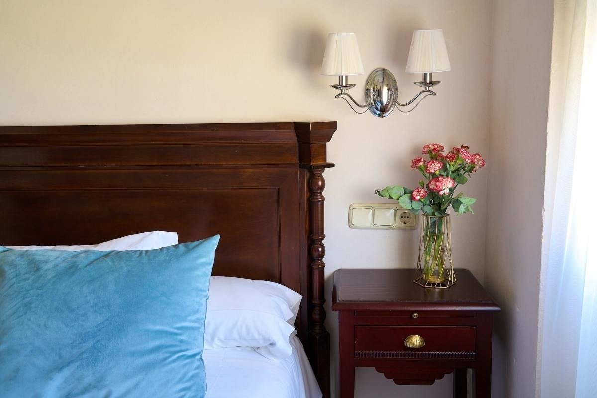 un jarrón de flores se sienta en una mesita de noche junto a una cama