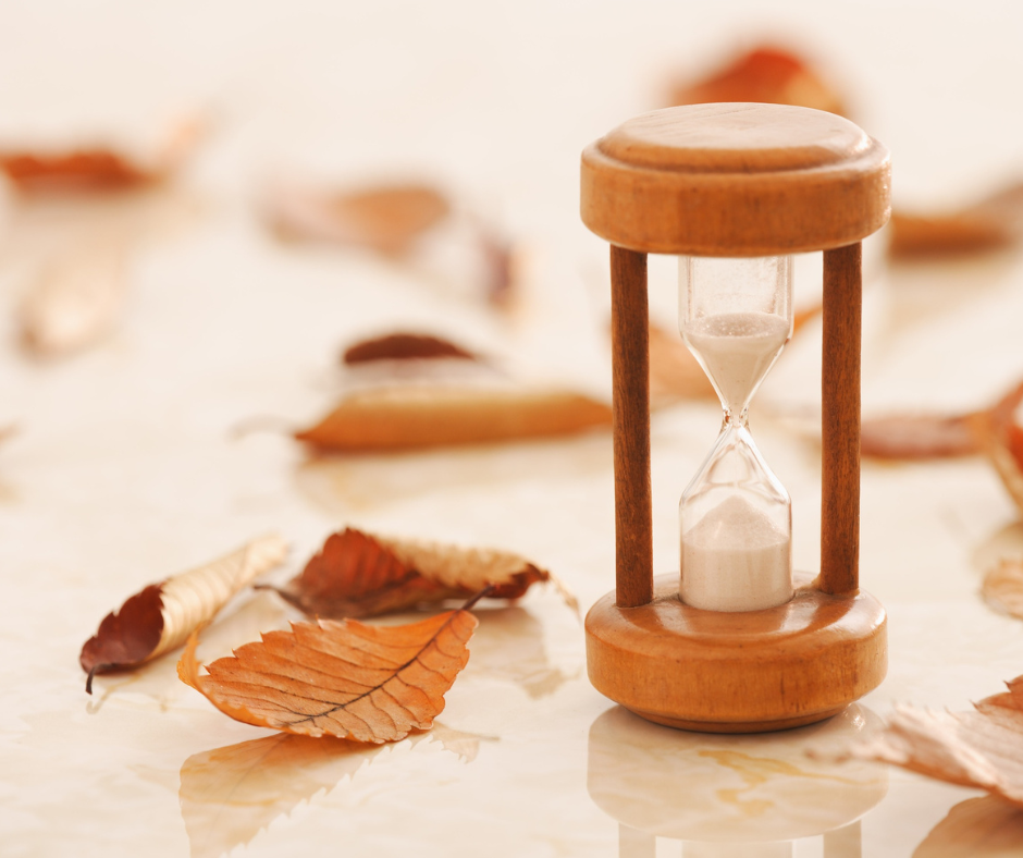 un reloj de arena de madera está sobre una mesa junto a hojas secas