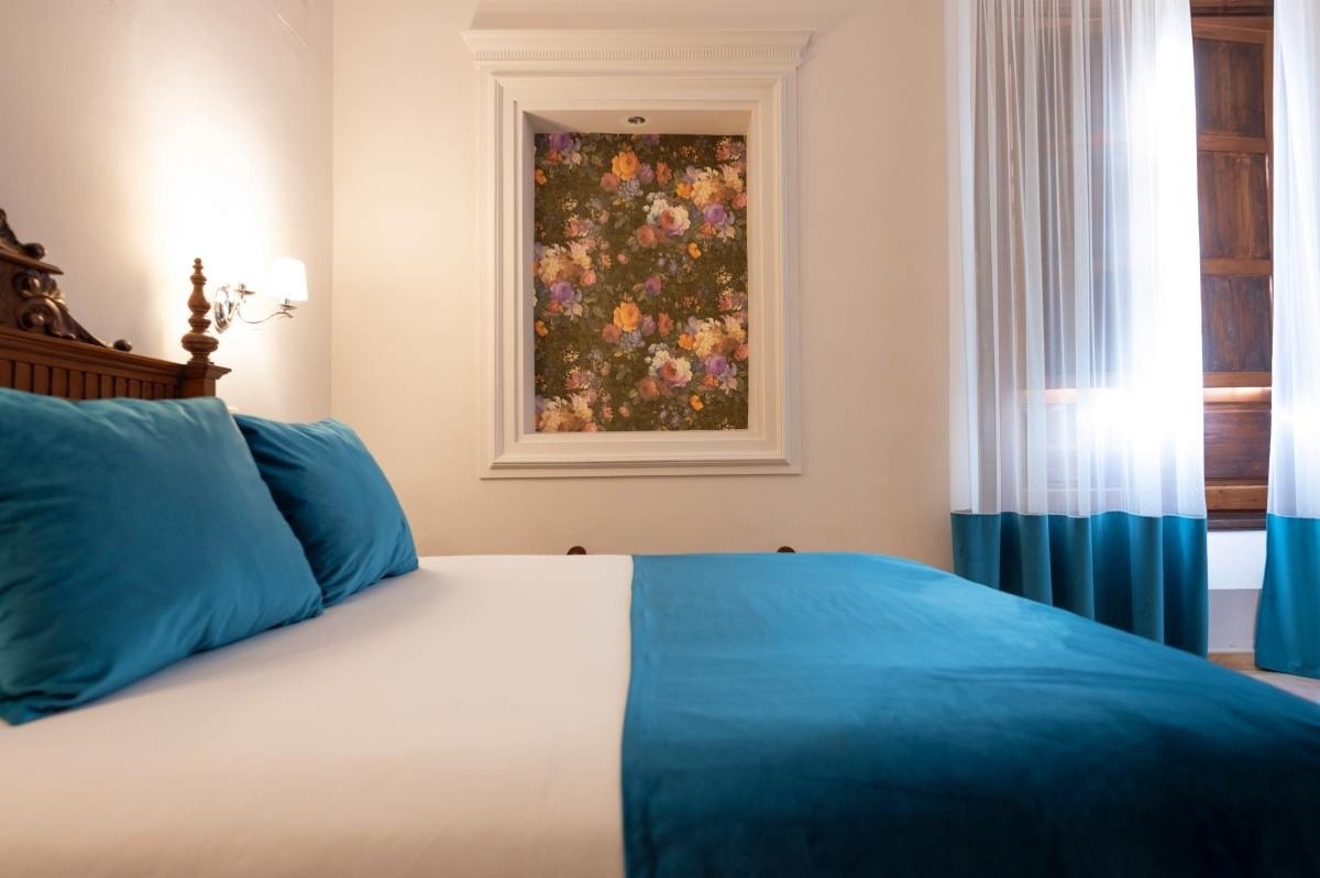 una habitación con una cama y una ventana con una pintura floral en la pared