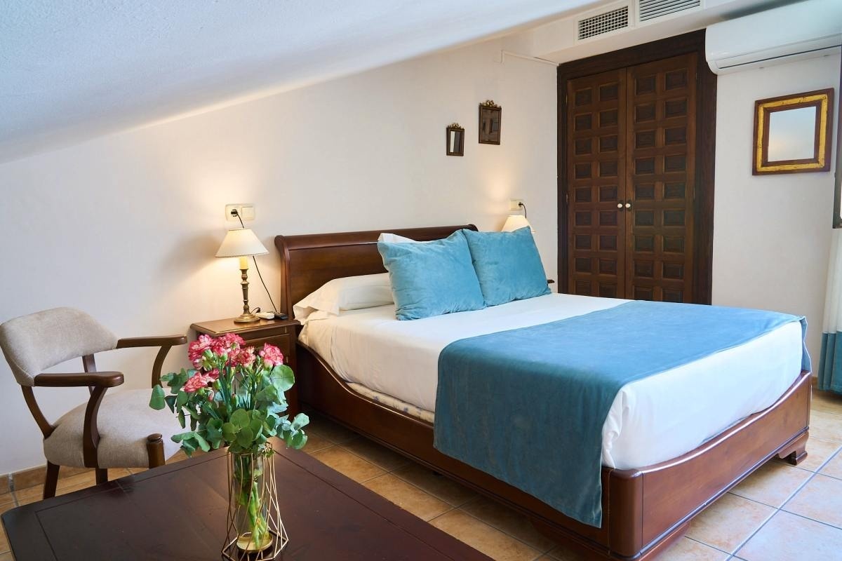 una habitación con una cama y una silla y un jarrón de flores