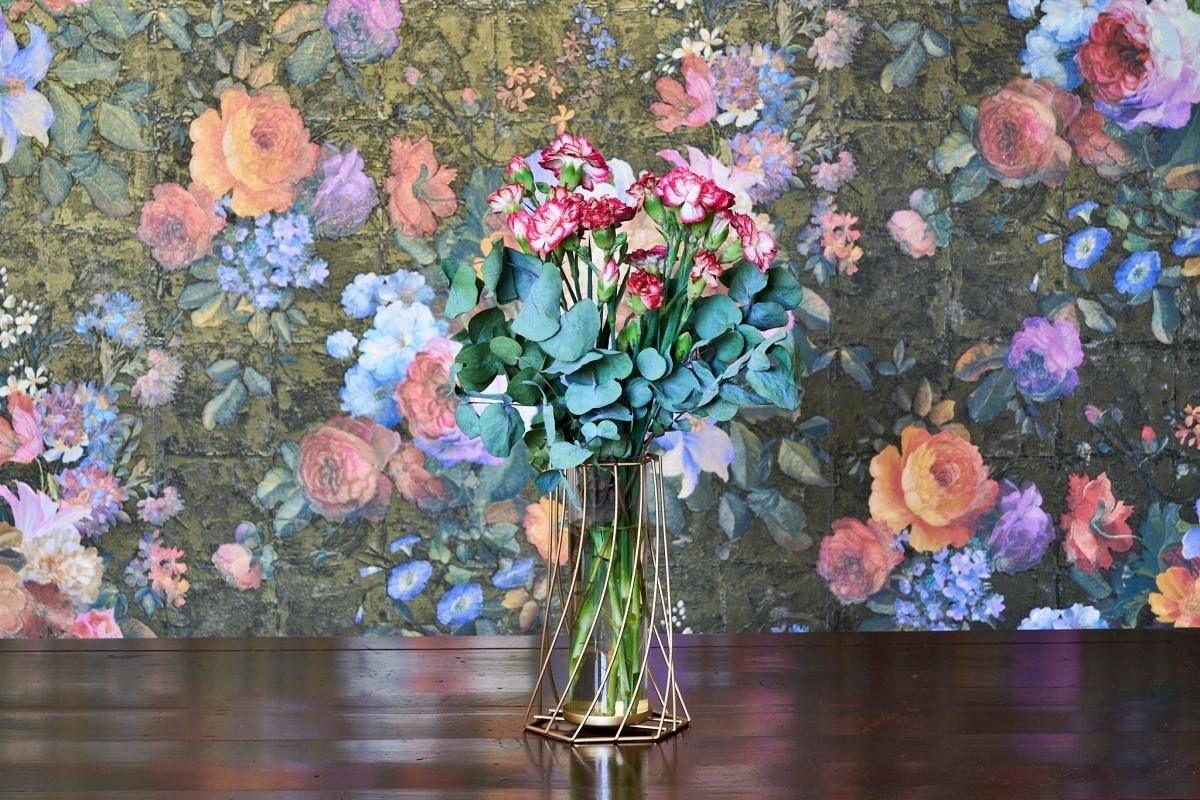 un jarrón lleno de flores está sobre una mesa frente a un fondo de flores