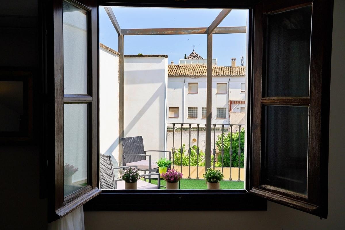 una ventana abierta con una silla y macetas en el balcón