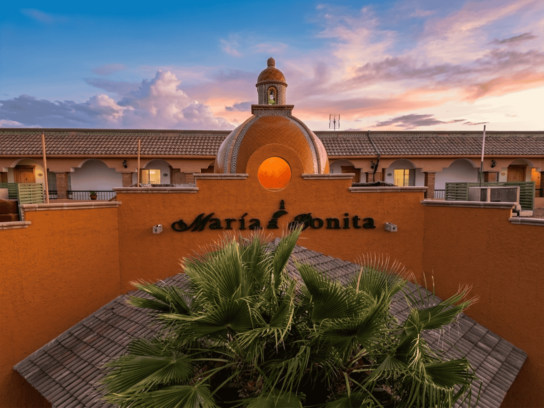 Edificio corporativo de "Maria Bonita" con cúpula naranja y palmeras. Ideal para negocios.