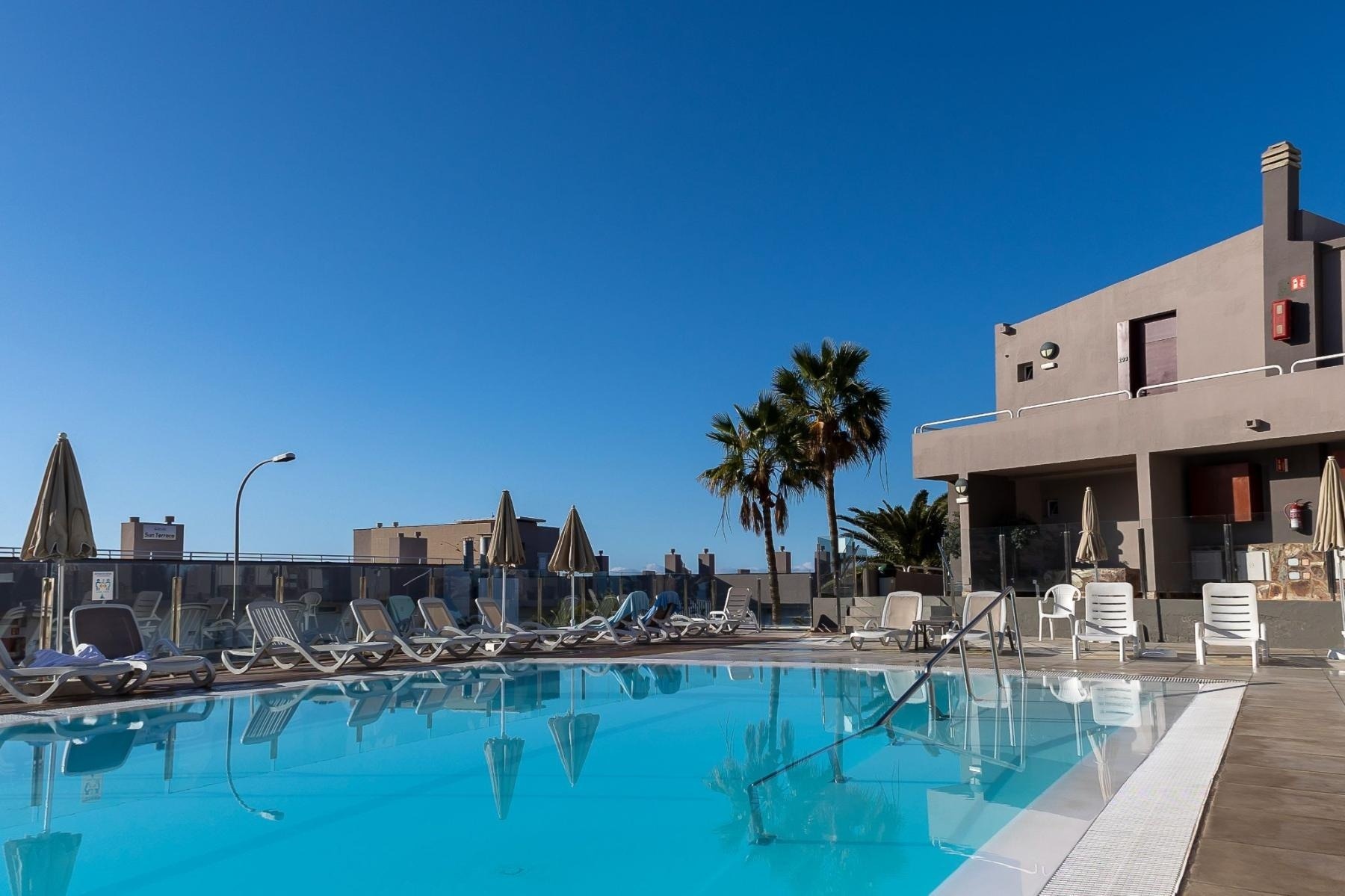 una piscina rodeada de sillas y sombrillas con un edificio en el fondo