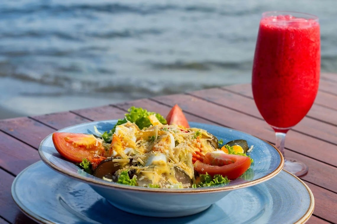 Ensalada fresca y bebida roja en mesa de madera junto al mar en Marina Puerto Velero.