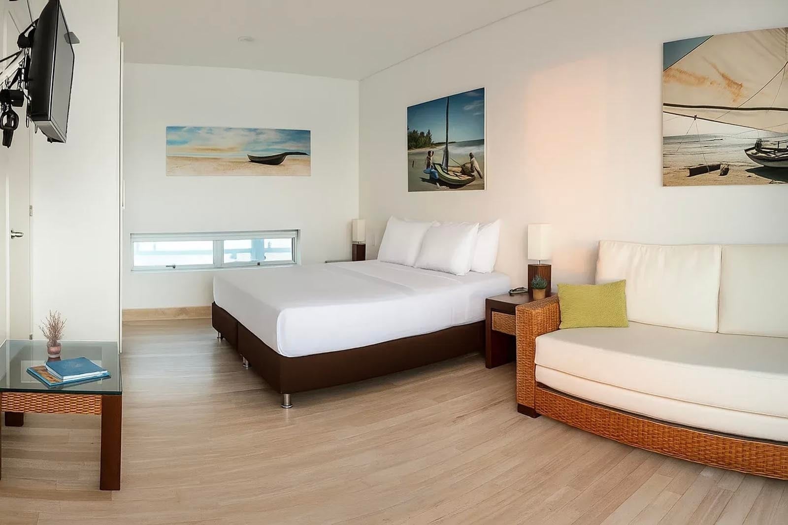 Habitación luminosa con cama, sofá y arte costero en Marina Puerto Velero.