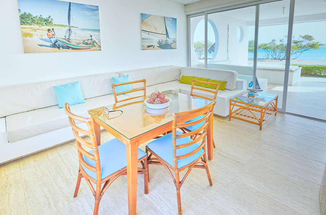 Marina Puerto Velero: sala de estar con vistas al mar, sofá blanco, mesa de comedor de cristal, sillas de mimbre y decoración playera.