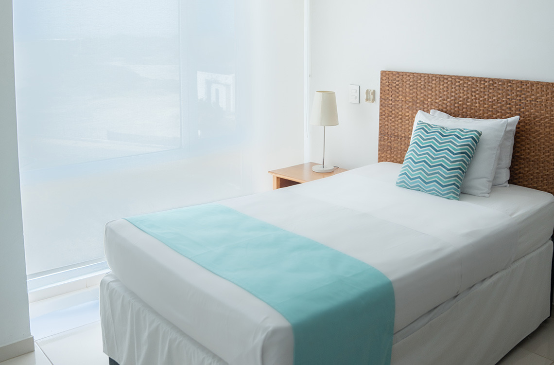Cama de hotel con cabecero de ratán y cojínMarina Puerto Velero.