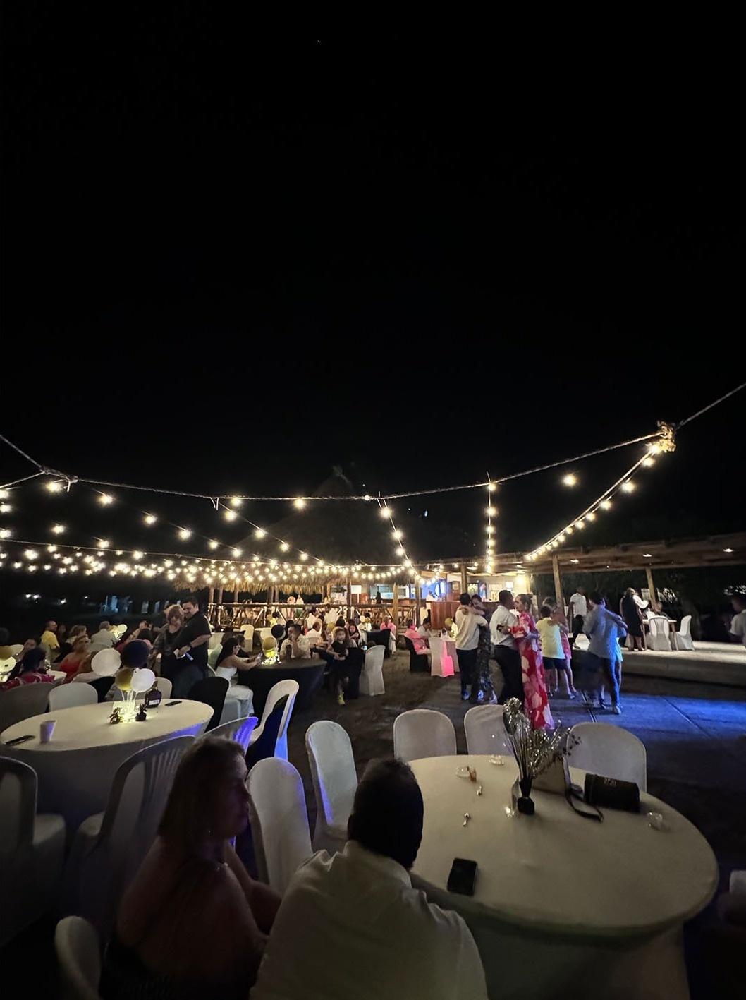 Noche de fiesta en Marina Puerto Velero con luces, mesas y gente bailando.