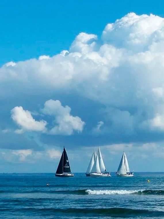Velero negro y blancos navegan en Marina Puerto Velero bajo nubes de algodón.