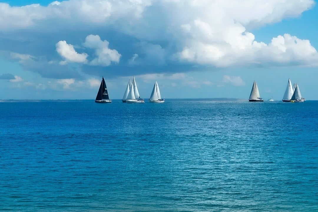 Sailboats race at Marina Puerto Velero under a cloudy sky.