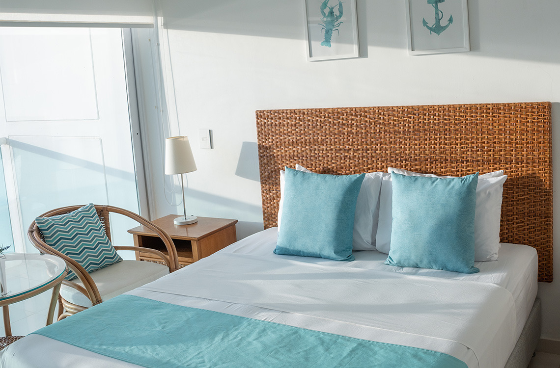 Cama con dosel de ratán y cojines azules. Marina Puerto Velero tropical.