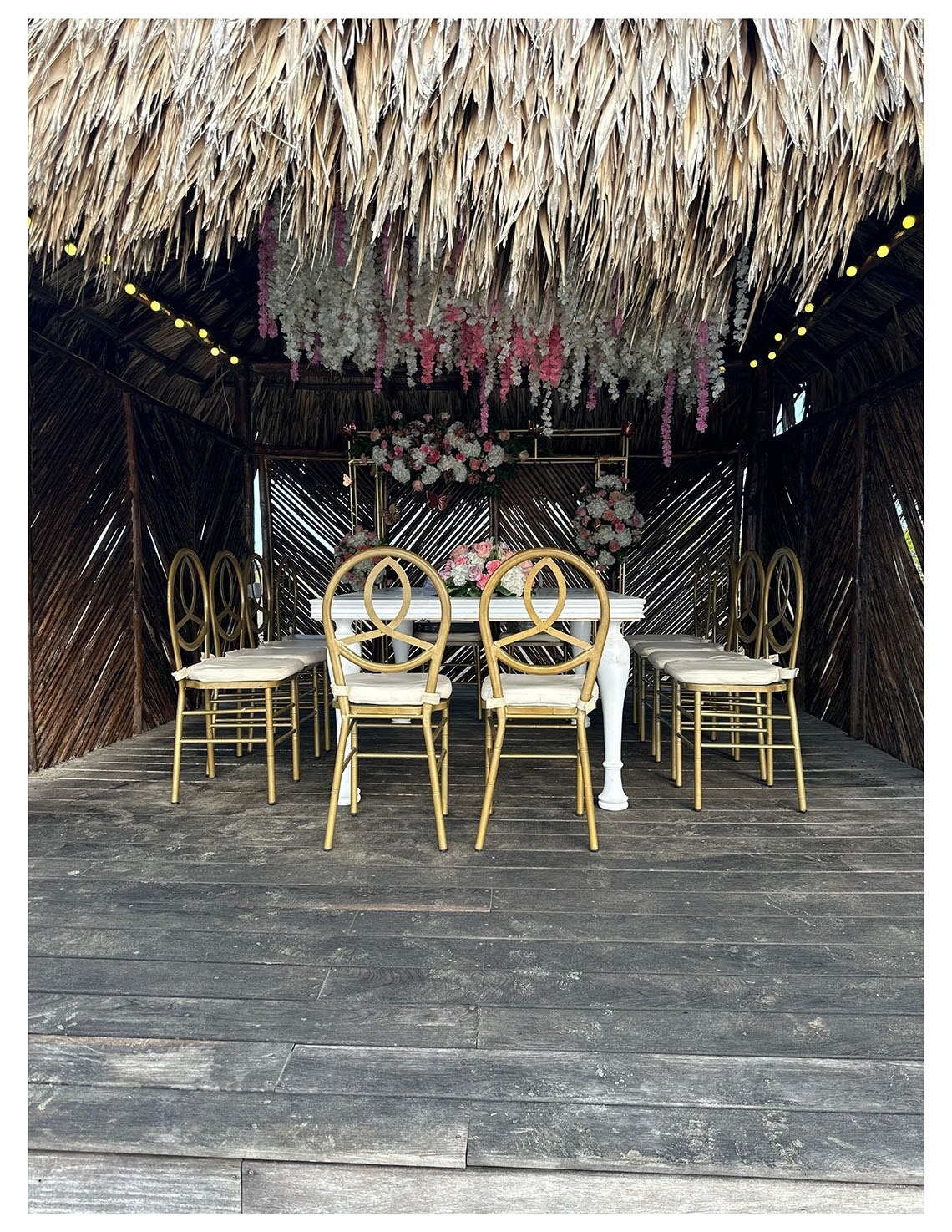 Mesa de bodas y sillas doradas bajo techo de paja en Marina Puerto Velero.