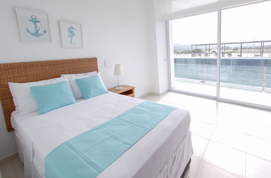 Habitación con cama turquesa y vista al mar en Marina Puerto Velero.