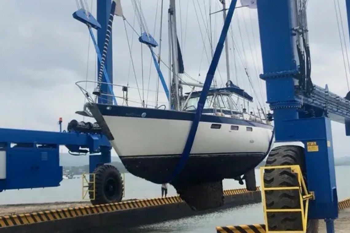 Sailboat lifted at Marina Puerto Velero, blue crane suspending white and blue yacht.