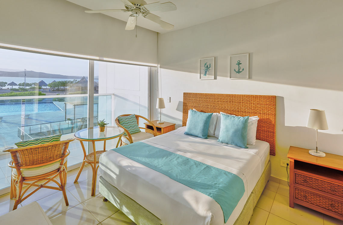 Habitación con cama queen, ropa de cama azul y blanca, y vista al mar en Marina Puerto Velero.