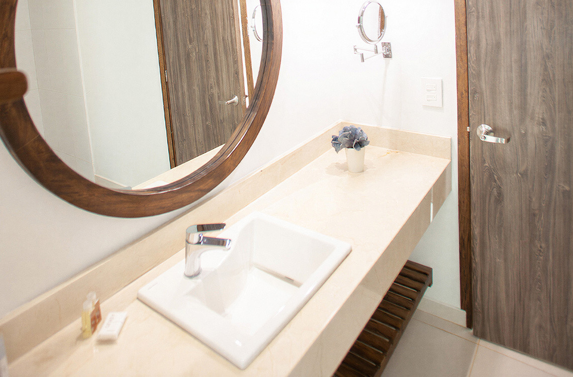 Baño moderno con lavabo, espejo redondo y puerta de madera. Marina Puerto Velero para una estancia confortable.