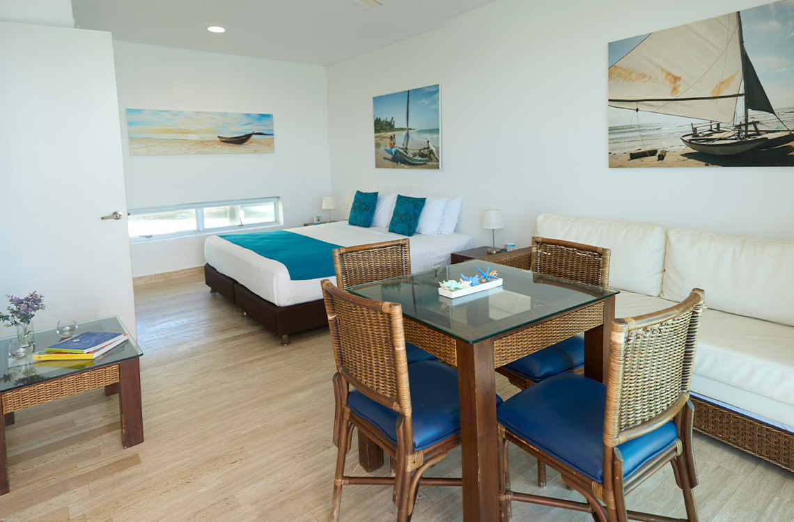 Amplia habitación de hotel con cama doble, sofá y mesa de Marina Puerto Velero con vista al mar.