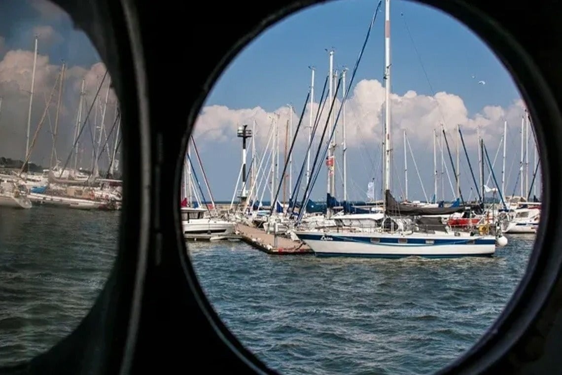 Sailboats docked at Marina Puerto Velero, seen through a porthole window.