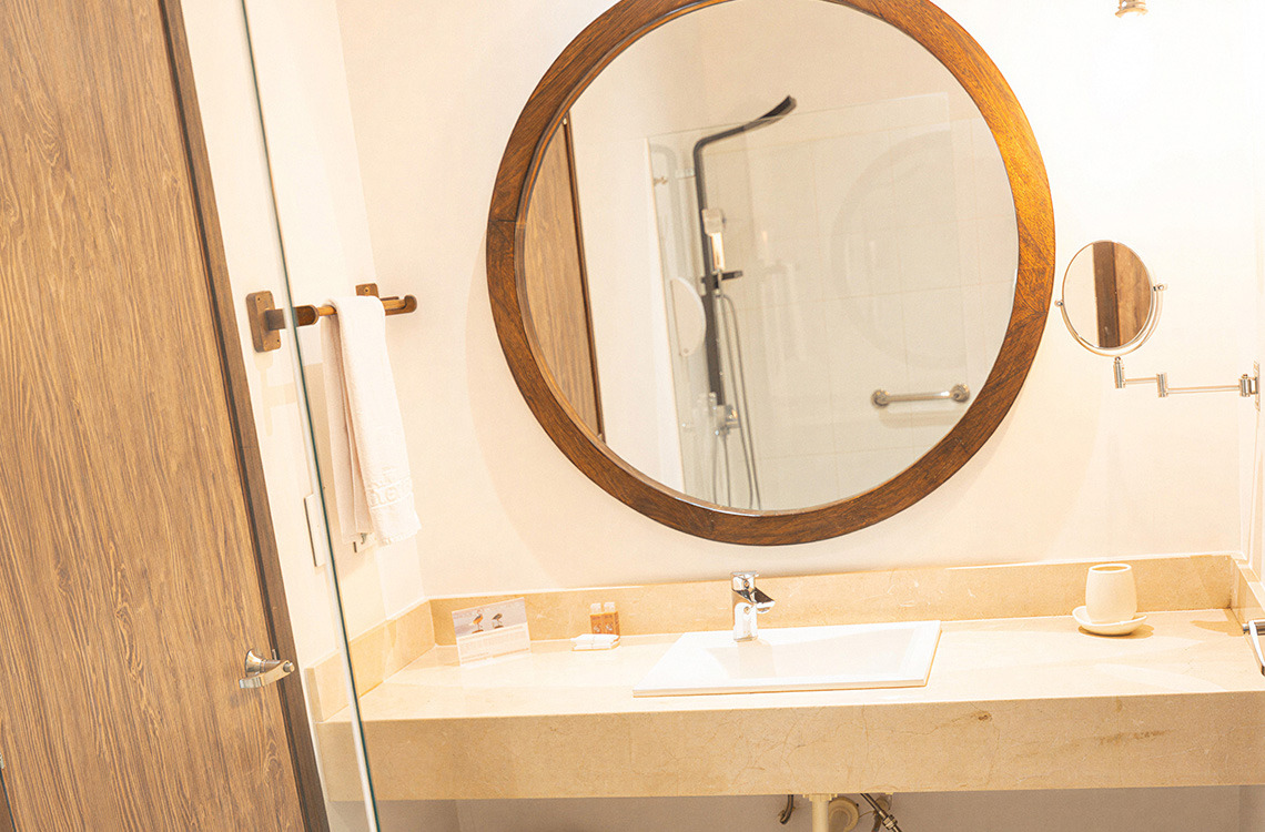 Espejo redondo con marco de madera en baño moderno, lavabo y toalla. Marina Puerto Velero