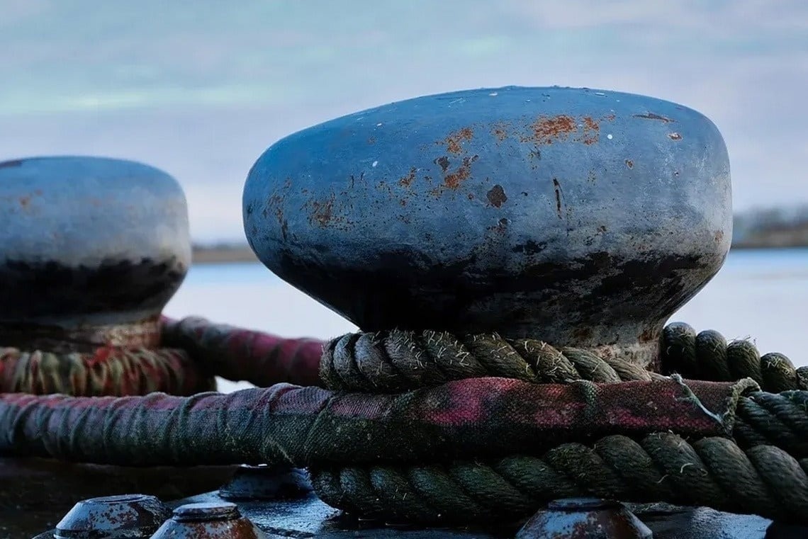 Blue bollard at Marina Puerto Velero with thick ropes and rust.