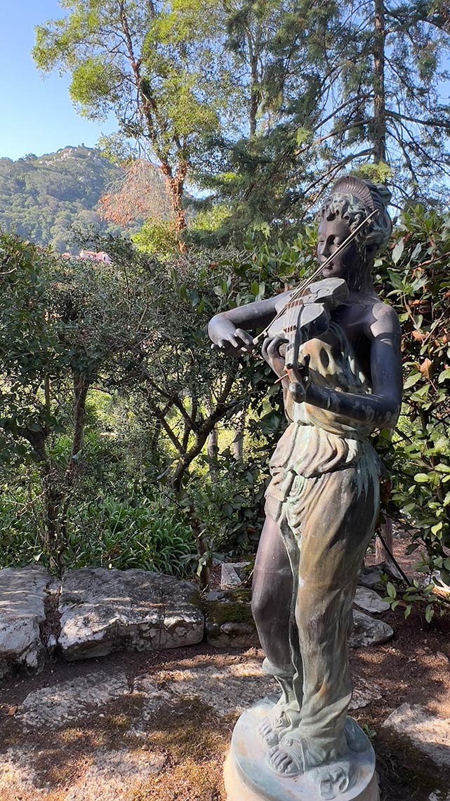 Estátua de bronze de uma mulher tocando violino em um jardim exuberante, ideal para Marmoris: Corporative.