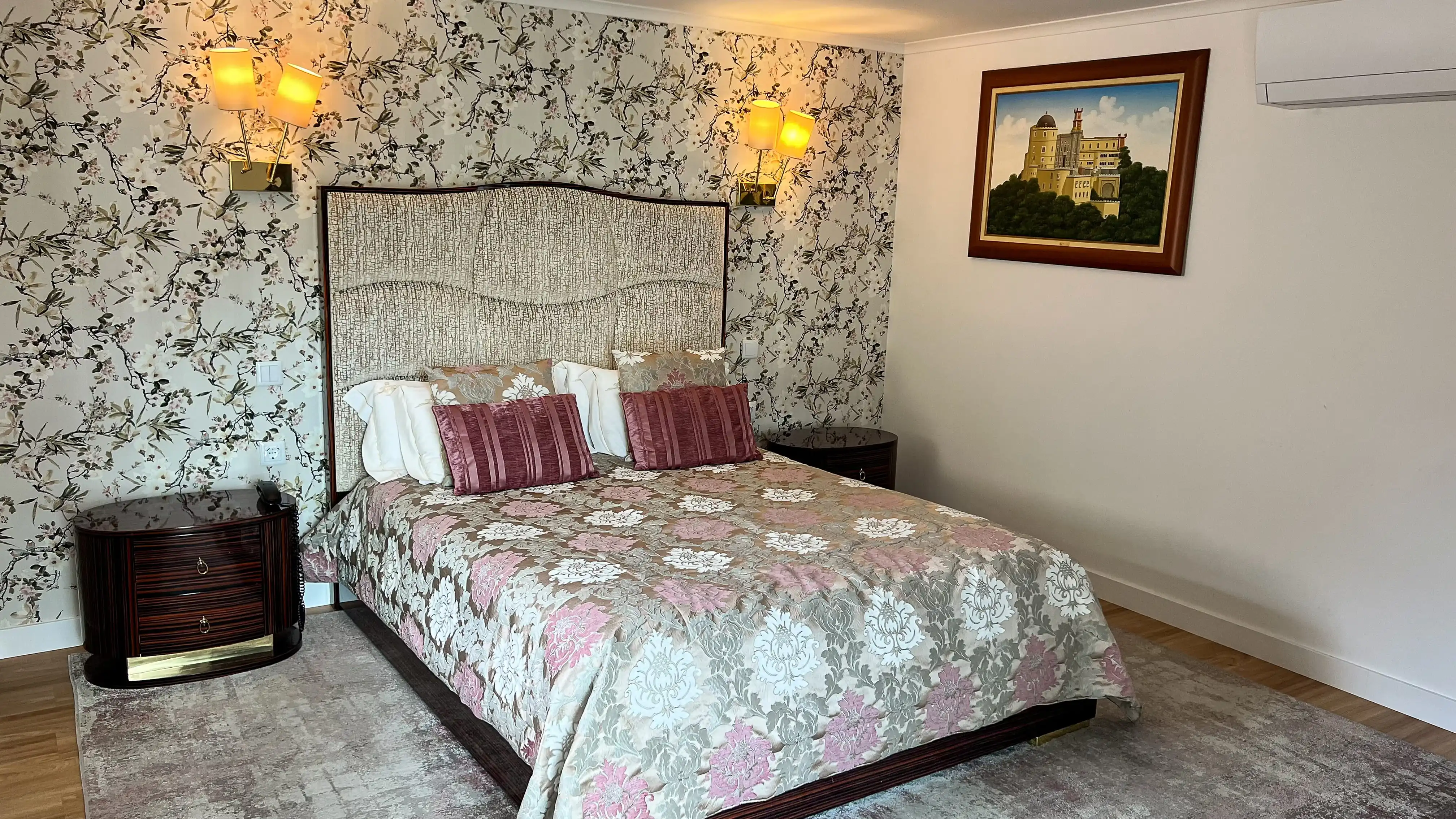 Quarto de hotel com papel de parede floral, cama king-size Marmoris Hotels, mesas de cabeceira e pintura de castelo.