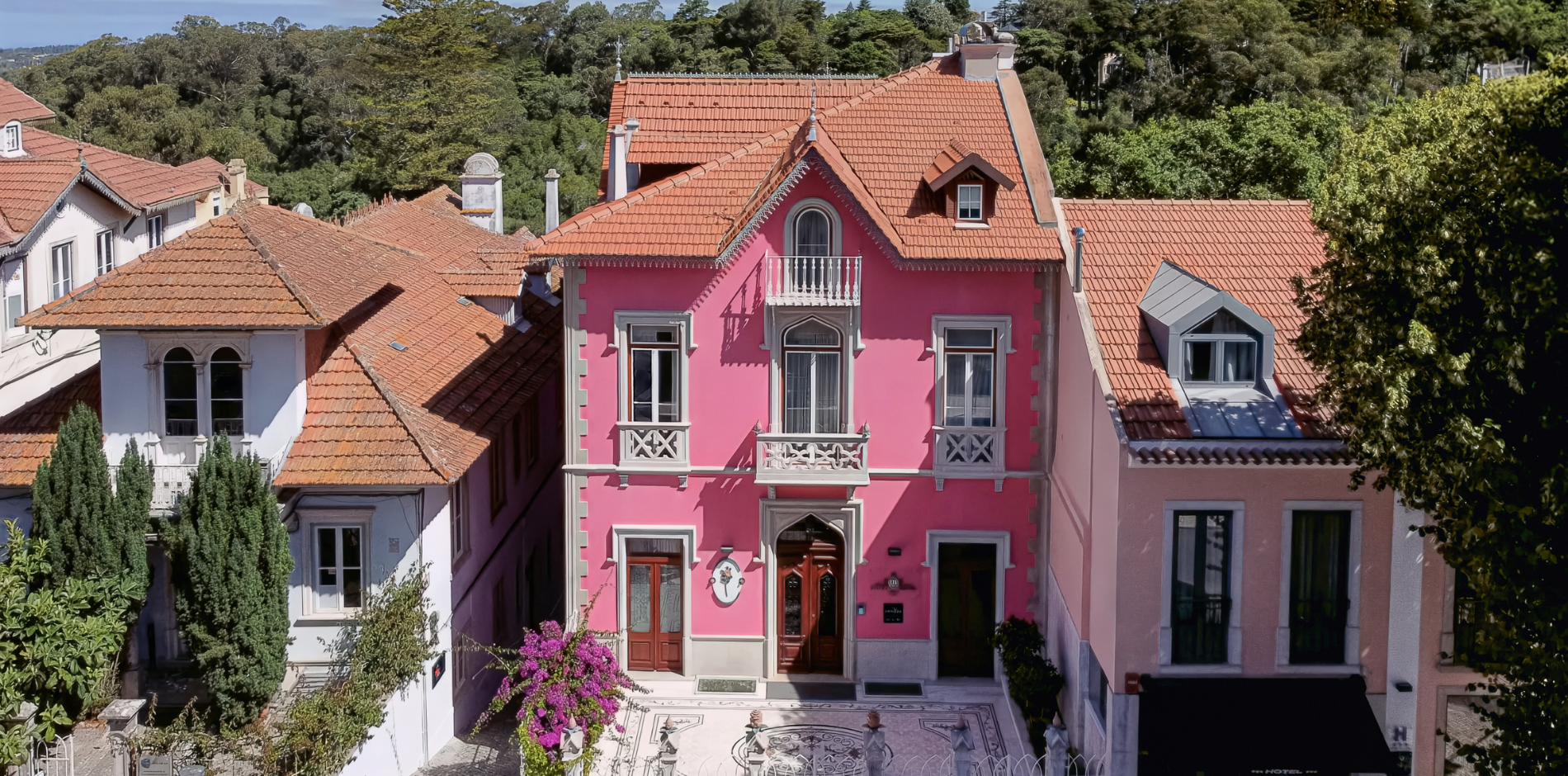 una casa rosa con un techo de tejas rojas está rodeada de otras casas