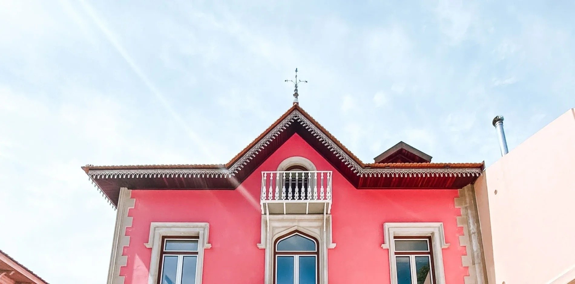 una casa rosa con un techo de tejas rojas está rodeada de otras casas