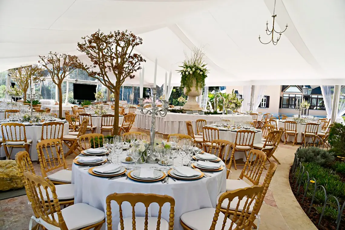 Elegant wedding tent Marmoris Hotels setup with round tables, golden chairs, and floral centerpieces.