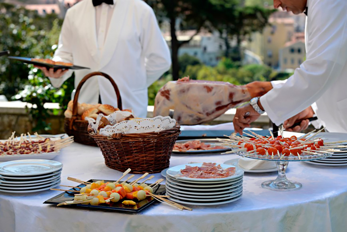 Banquete ao ar livre com garçons, presunto e espetos de frutas, perfeito para eventos em hotel. Marmoris: Corporative